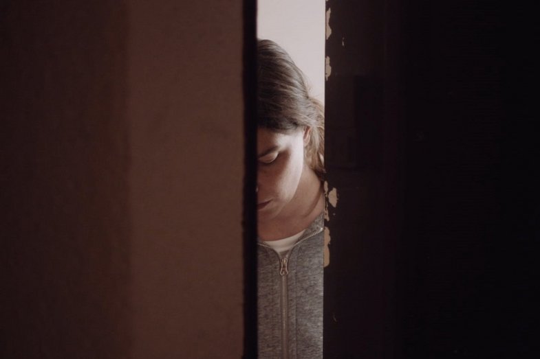 View through an open door of a person in a gray sweater.