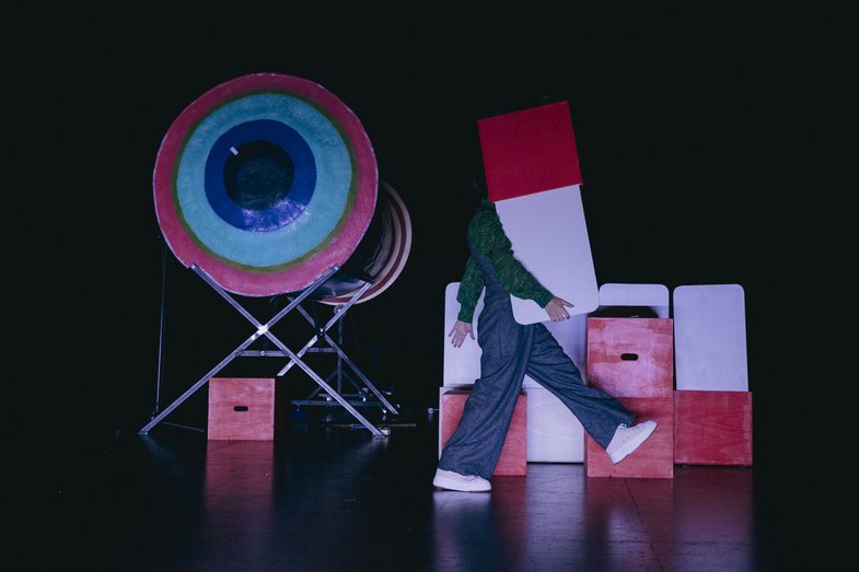 2.	A stage filled with props and one person holding a prop which is hiding their face