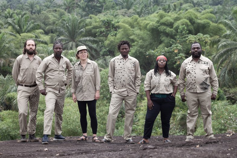Foto von sechs Personen, die in entspannter Haltung nebeneinander stehen und in die Kamera blicken, sie befinden sich auf einem Plateau, hinter ihnen erstreckt sich der Dschungel Kongos.  