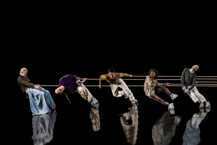 5 Personen ziehen an einem Seil und stehen auf einer verspiegelten Bühne