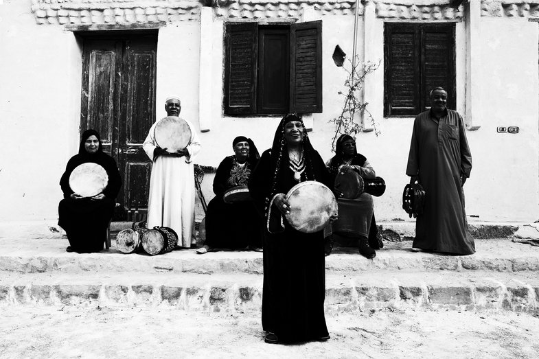 Photograph of people in front of a house. They are holding their instruments and looking at the camera.