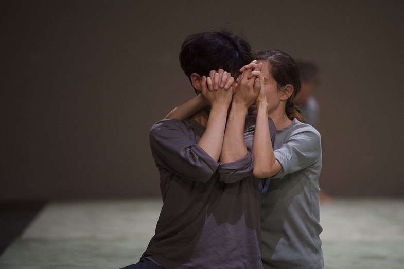 Photograph of two people covering their faces with their hands. Their hands are intertwined.