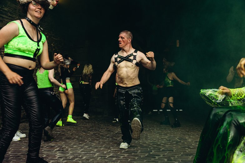 Several people, some with and without animal masks, dance in a dark club-style room.