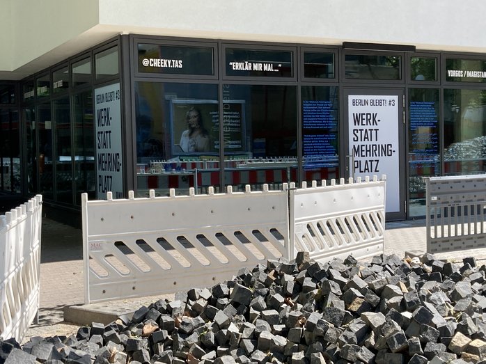 A photo of the shop window in the vacant shop with HAU posters. A construction site in the foreground.