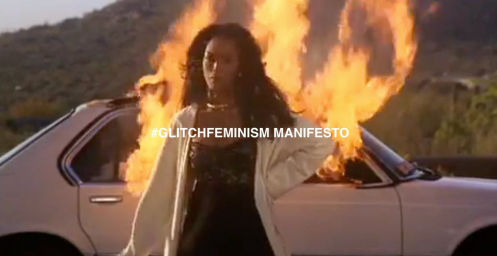 A black woman stands in front of a burning car. The words "#Glitchfeminism Manifesto" in front of it.