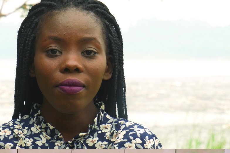 A woman with braids looks directly into the camera.