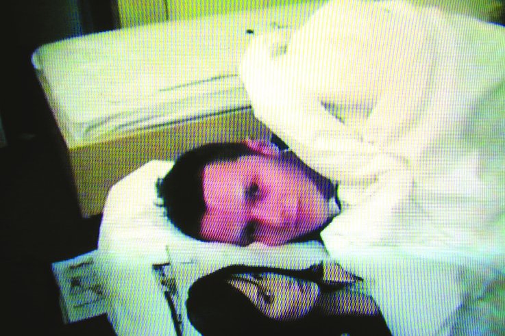Ein Ausschnitt aus einem Video, das einen Mann im Bett zeigt, der unter einer Decke neben dem Bild einer Frau liegt.