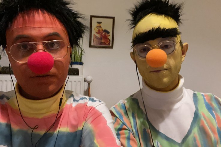 Ein Selfie von zwei Personen, die als Ernie und Bert aus der Sesamstraße verkleidet sind. Im Hintergrund ist ein gerahmtes Bild von den Originalfiguren. 
