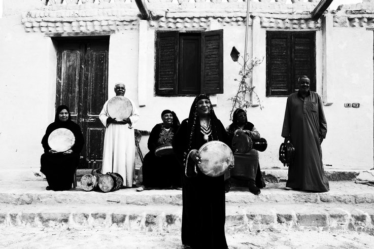 Photograph of people in front of a house. They are holding their instruments and looking at the camera.