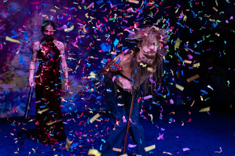Two people stand on a stage surrounded by confetti that flies around in the air.