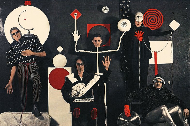 Photo of the band Vanishing Twin: Five people look towards the camera, various geometric shapes are found on the people and in the background.