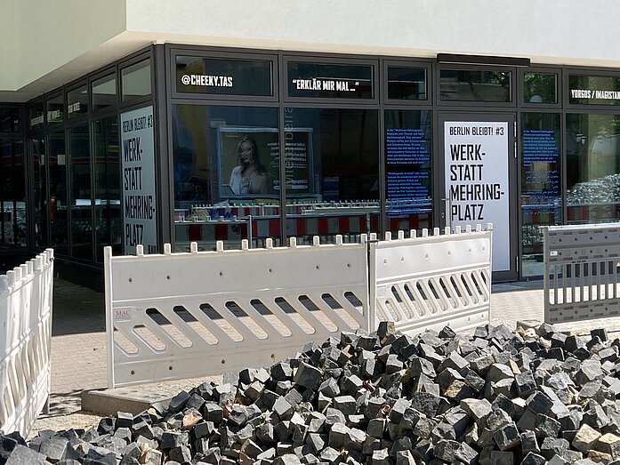 A photo of the shop window in the vacant shop with HAU posters. A construction site in the foreground.