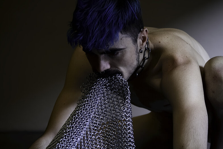 A topless person with blue hair and chainmail coming out of their mouth