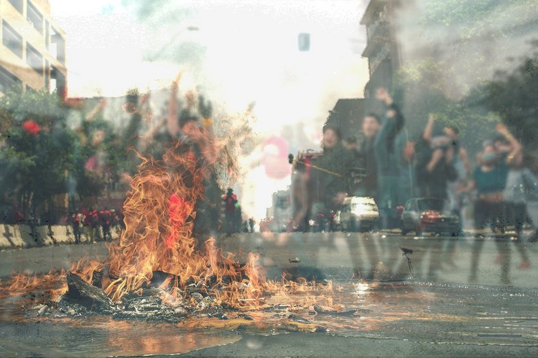 Auf einer Straße brennt ein Feuer. Davor oder dahinter jubelt eine Gruppe junger Menschen. 